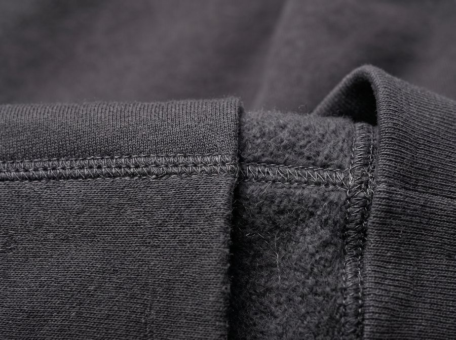 Extreme close-up of a fleece hem where the ribbed band meets the body, with the brushed loopback inner face visible at the fold