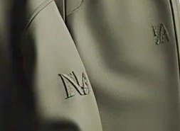 Close-up of a small tonal embroidered mark on an olive sweatshirt sleeve
